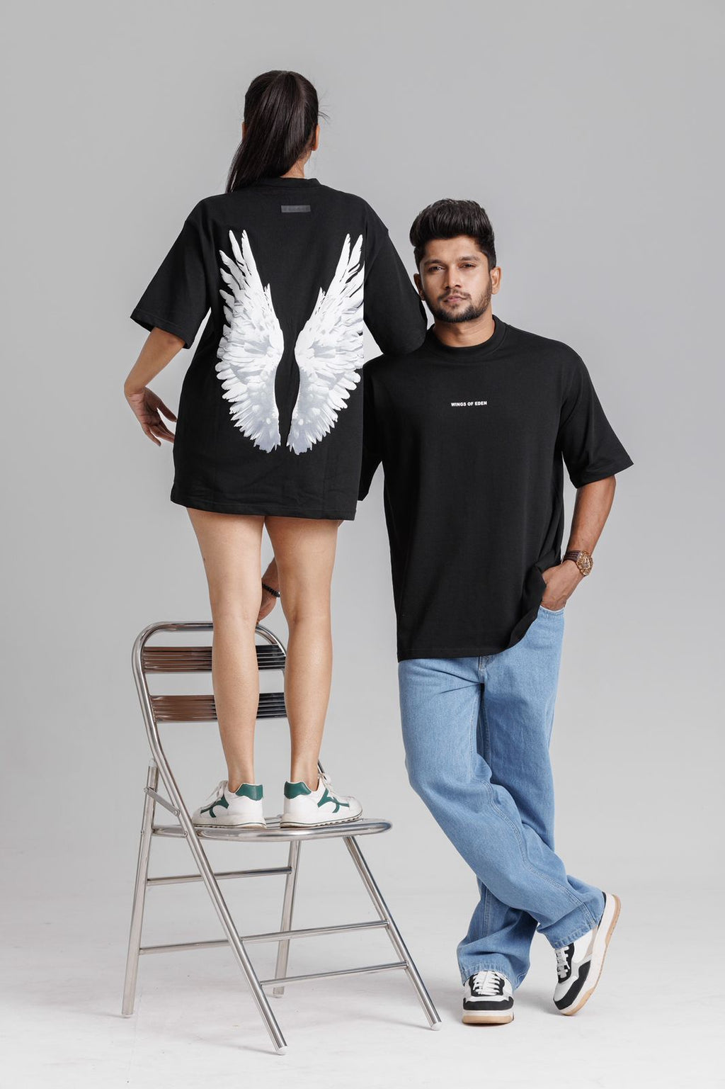 Two people wearing black t-shirts, one with wings design, on a plain background