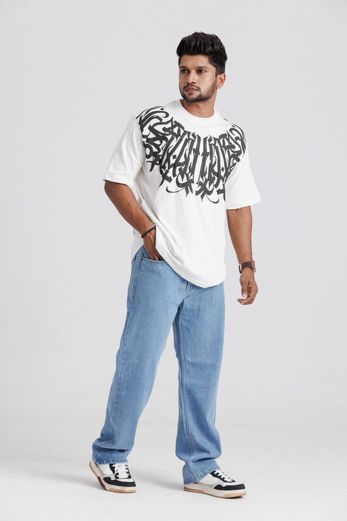Man wearing a white t-shirt with black graphics and blue jeans on a light gray background