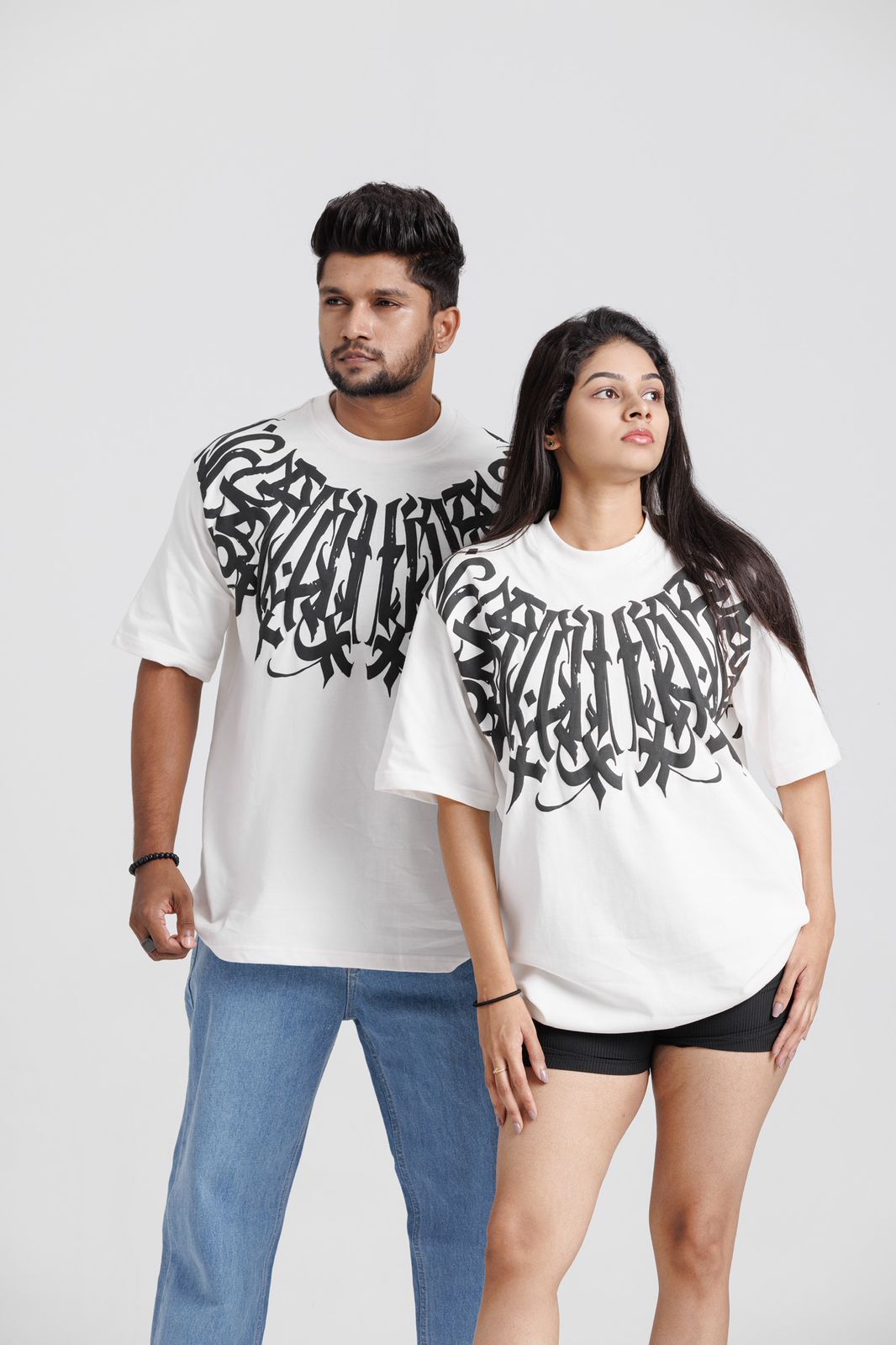 Two people wearing white t-shirts with black text design on a plain background