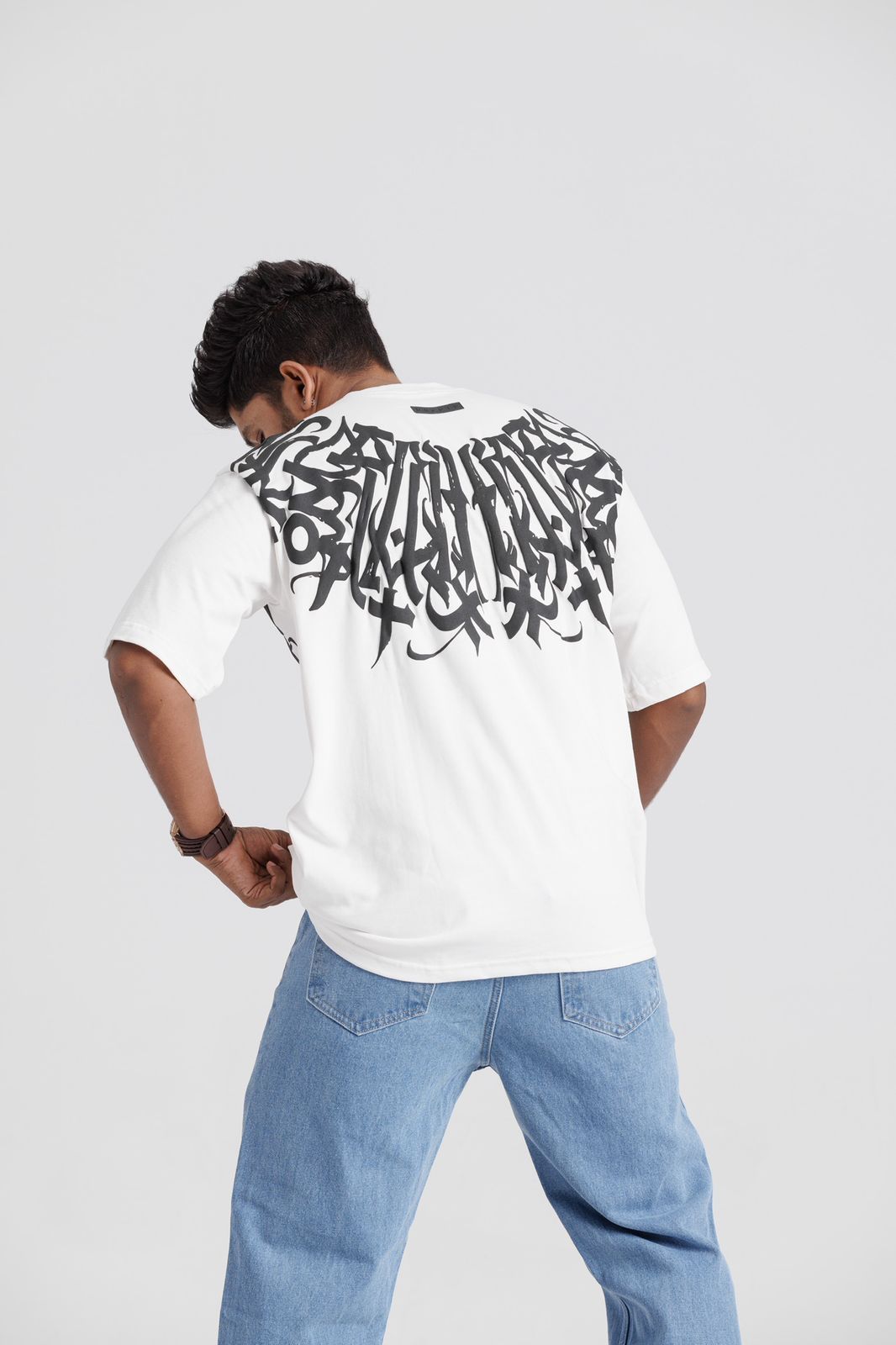 Person wearing a white t-shirt with black graphic design on the back, standing against a plain background.