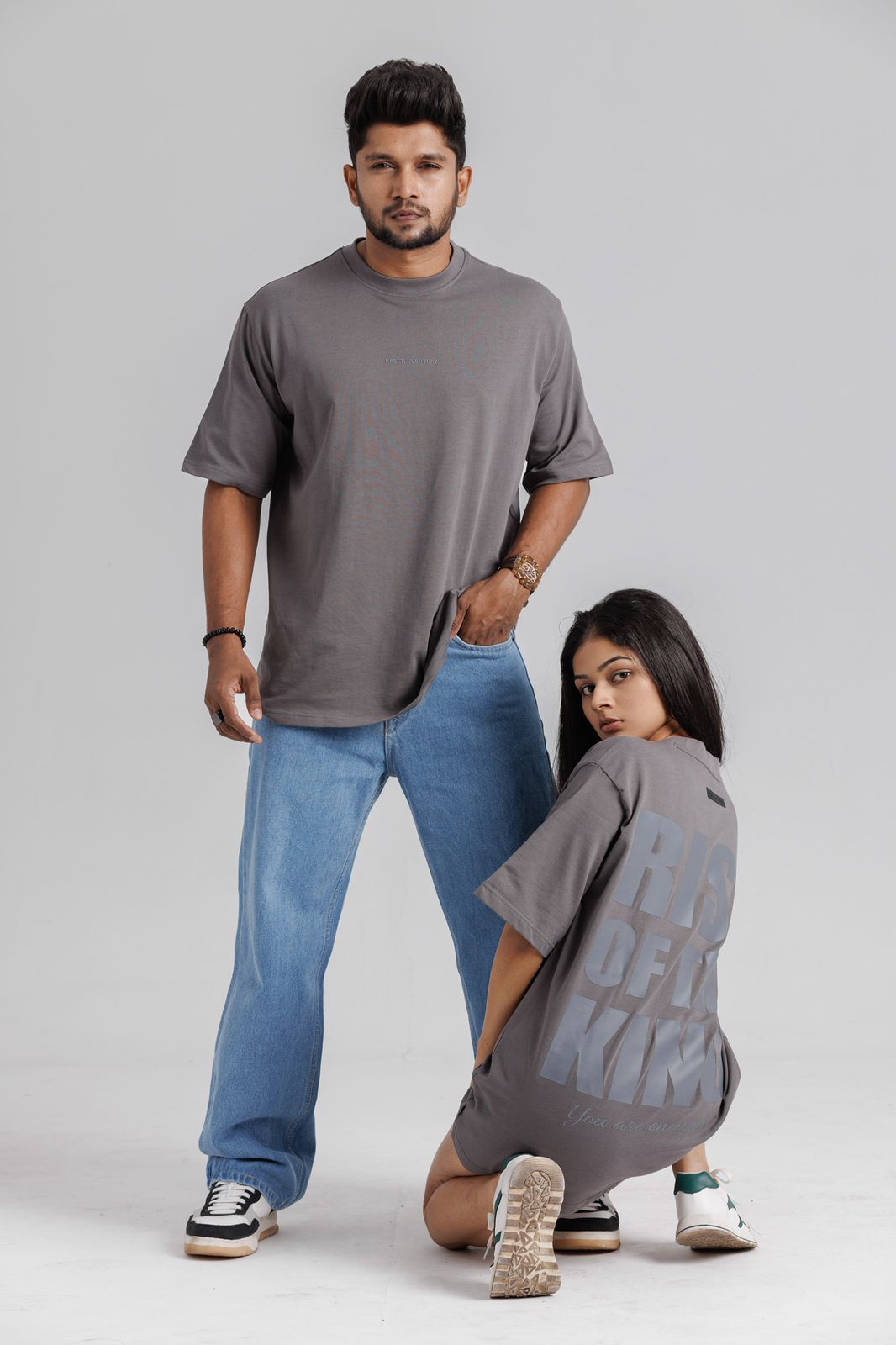 Two people wearing gray t-shirts and blue jeans on a plain background