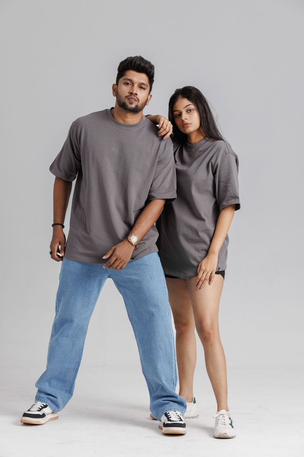 Two people wearing matching gray t-shirts and jeans on a plain background