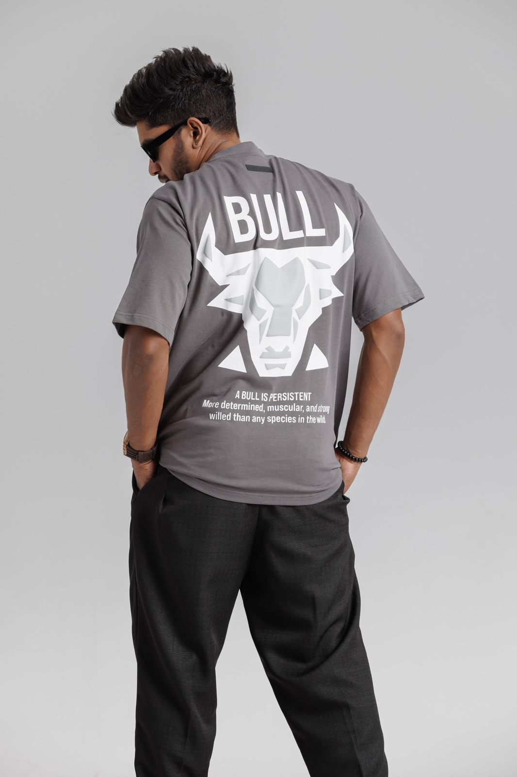 Person wearing a gray t-shirt with a bull graphic and text on the back, standing against a plain background.