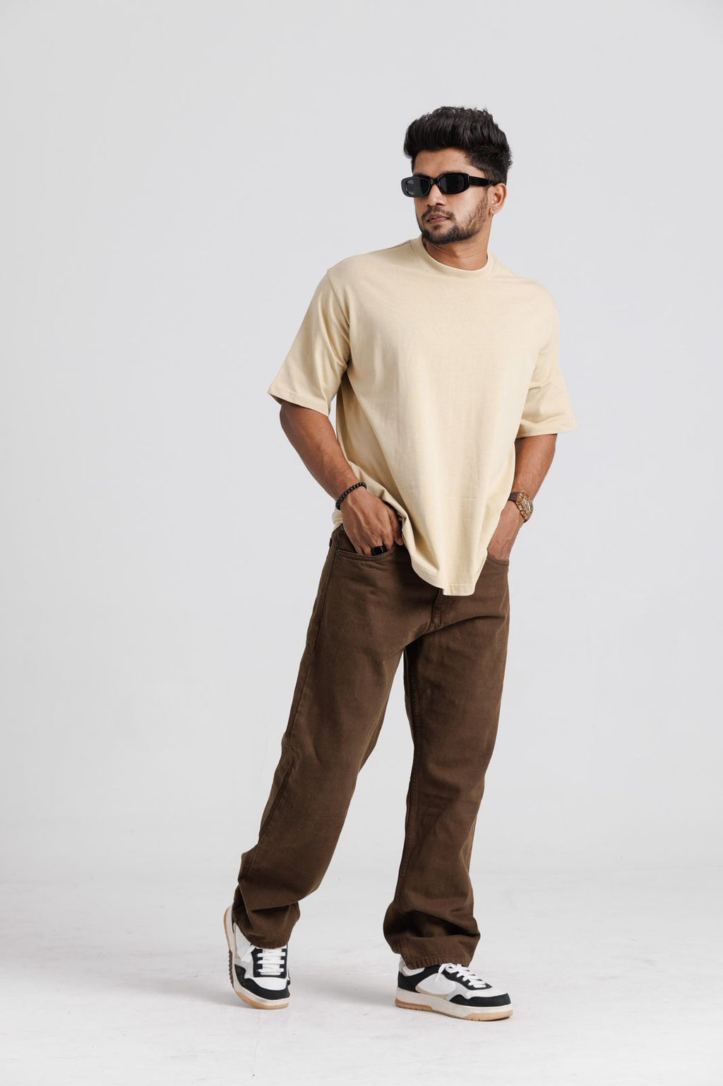 Man wearing a beige t-shirt and brown pants on a white background