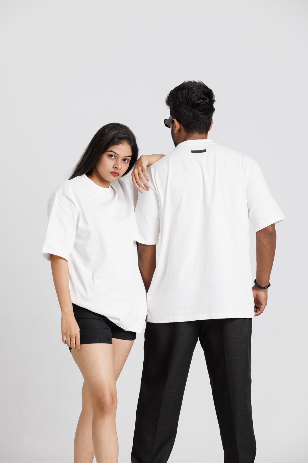 Two people wearing white t-shirts and black pants on a plain background