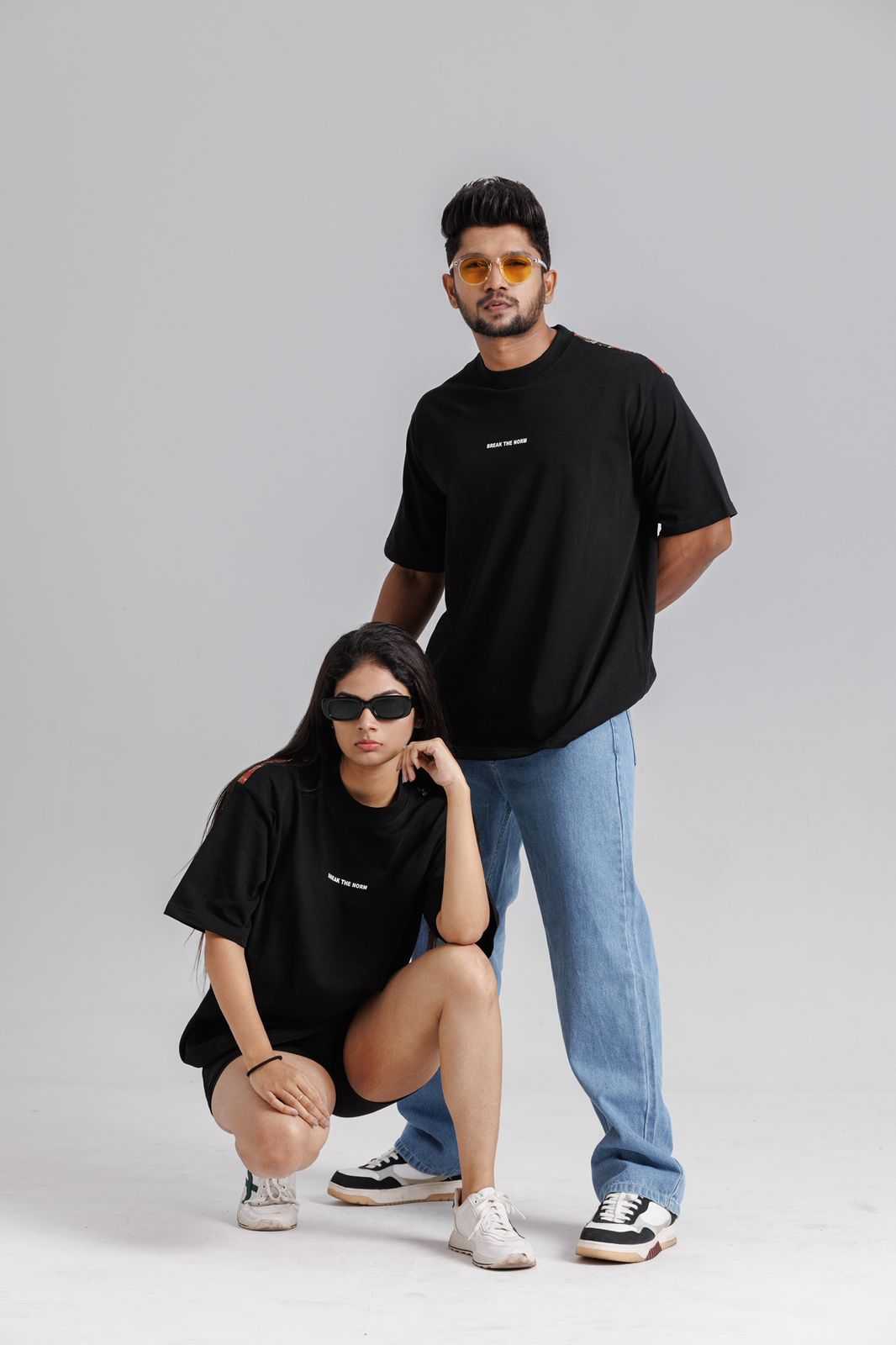 Two people wearing black t-shirts and sunglasses on a gray background