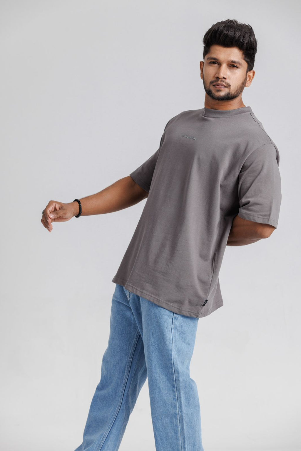 Man wearing a gray t-shirt and blue jeans on a plain background