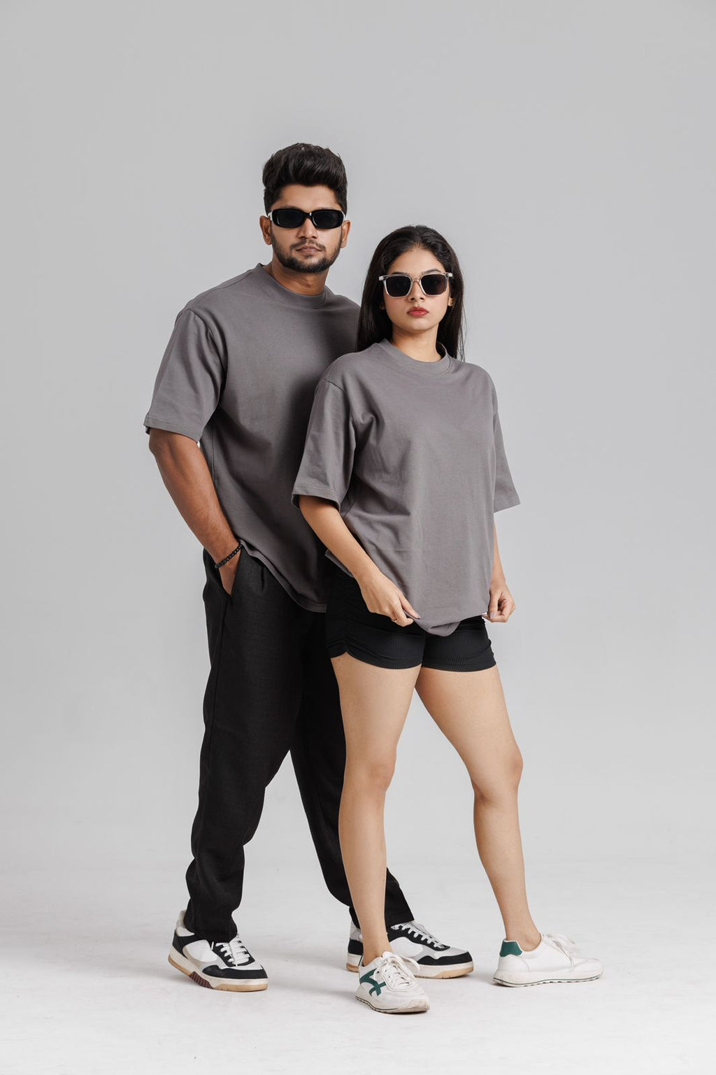 Two people wearing gray t-shirts and black pants on a plain background