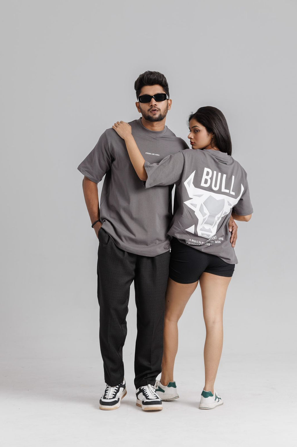 Two people wearing matching gray t-shirts with 'BULL' branding on a plain background