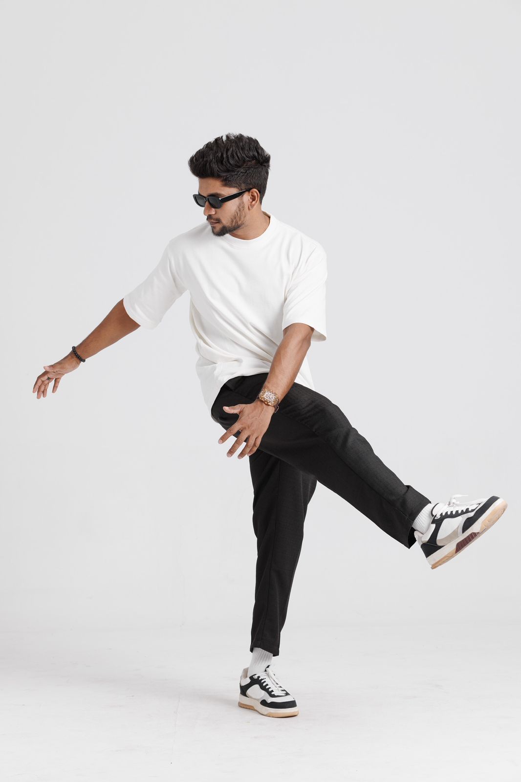 Man wearing a white t-shirt, black pants, and black and white sneakers on a white background