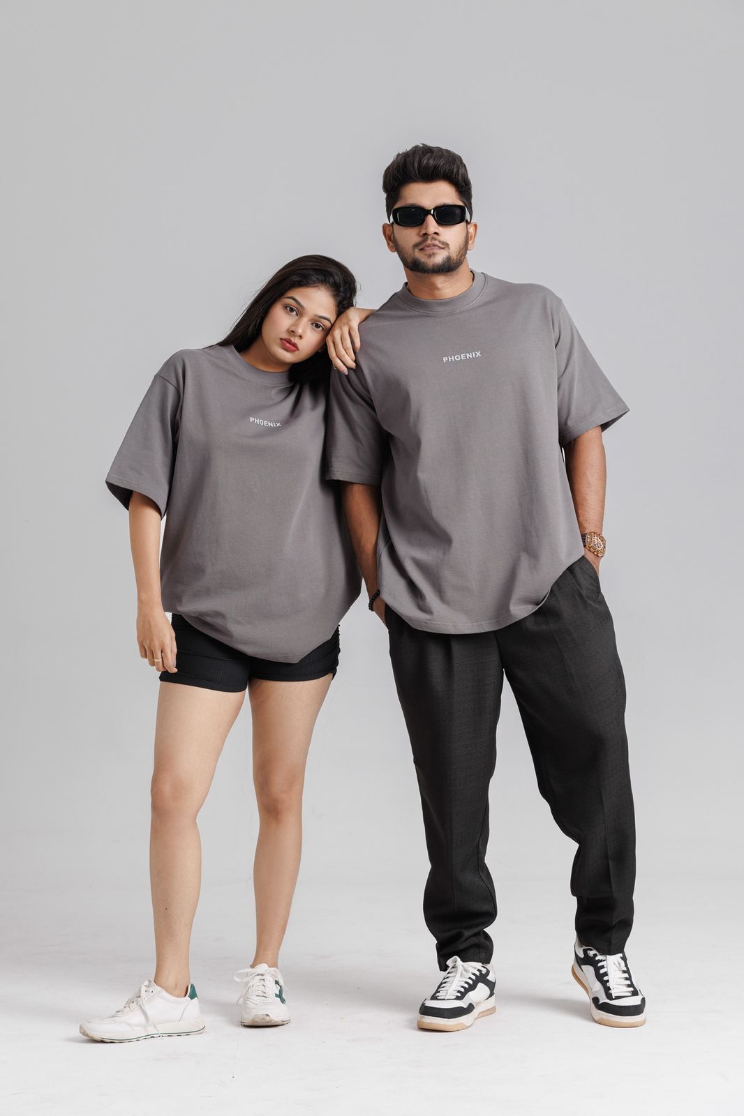 Two people wearing matching gray t-shirts and black pants on a plain background