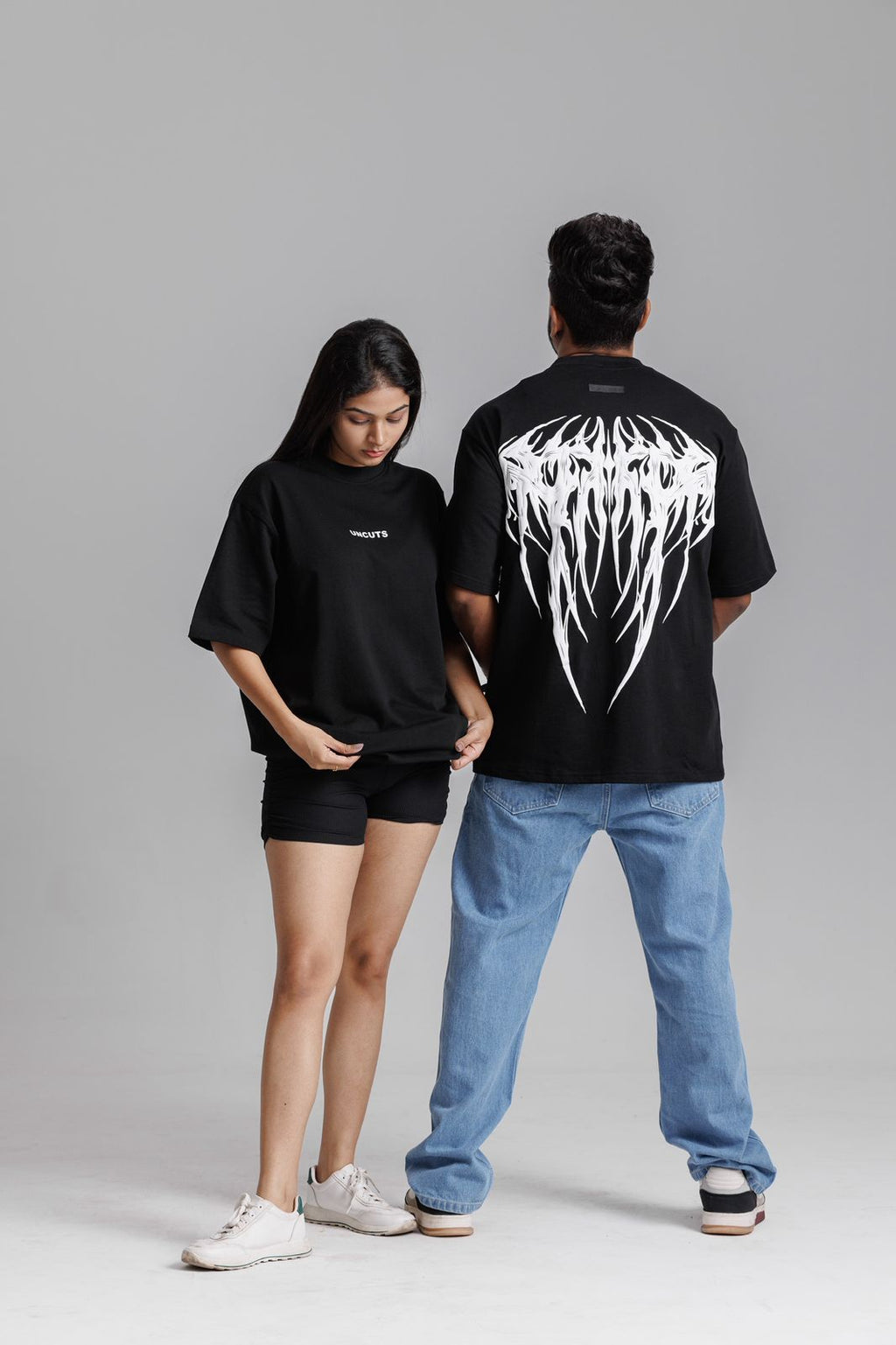 Two people wearing black t-shirts with white graphics on a gray background