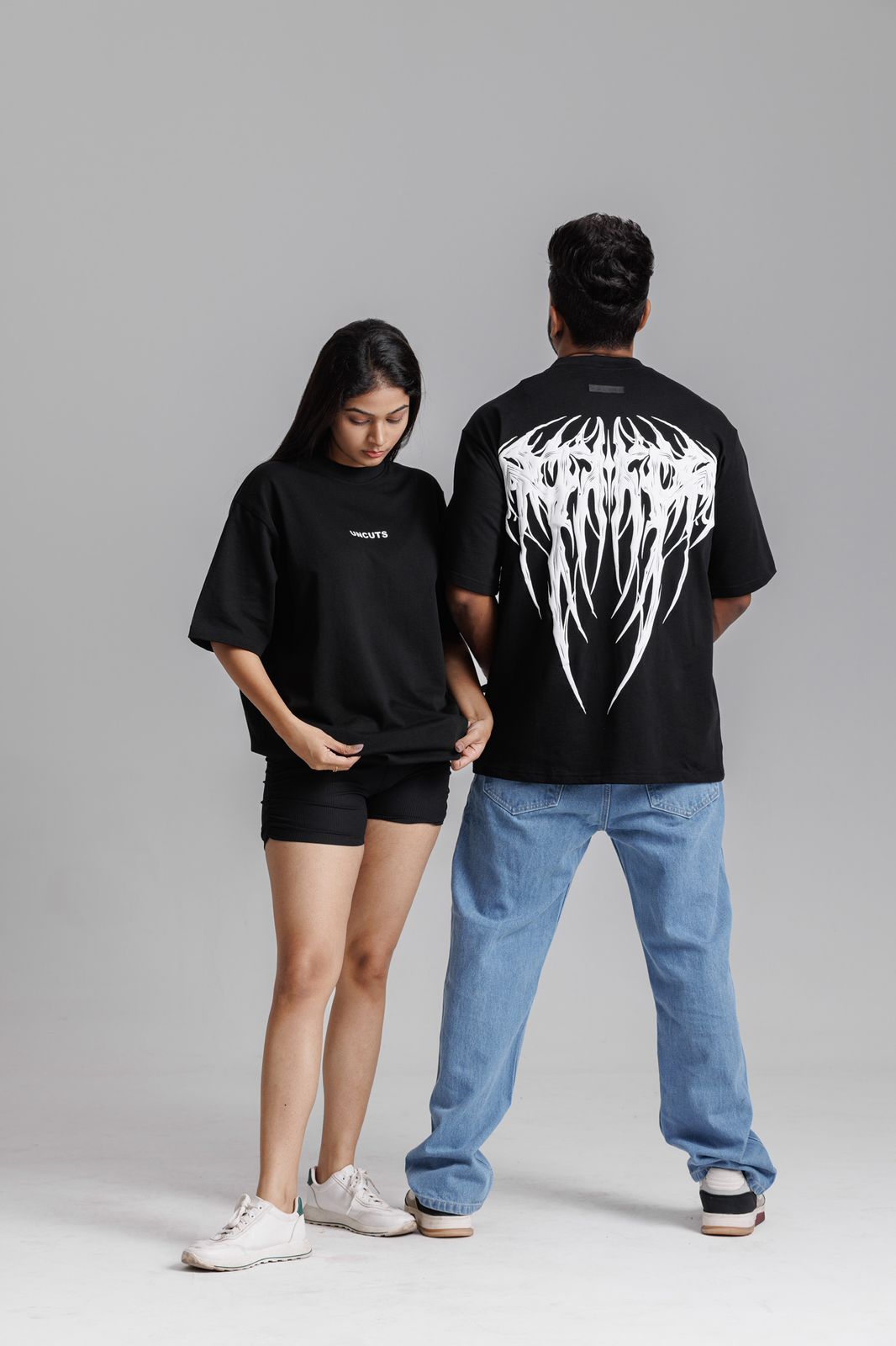 Two people wearing black t-shirts with white graphics on a gray background