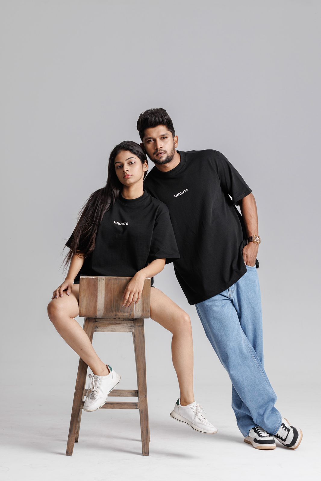 Two people wearing black t-shirts with visible branding against a gray background