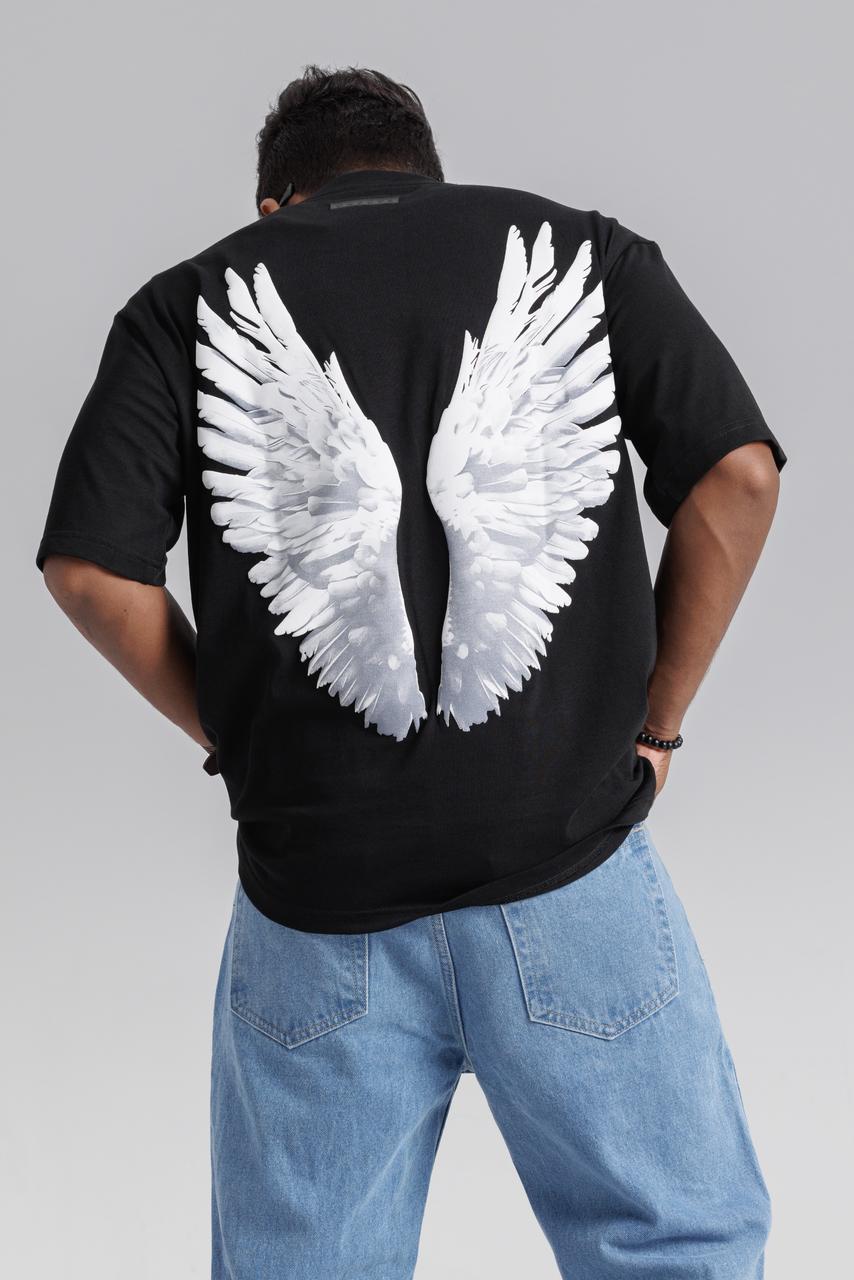 Person wearing a black t-shirt with white angel wings on the back against a gray background