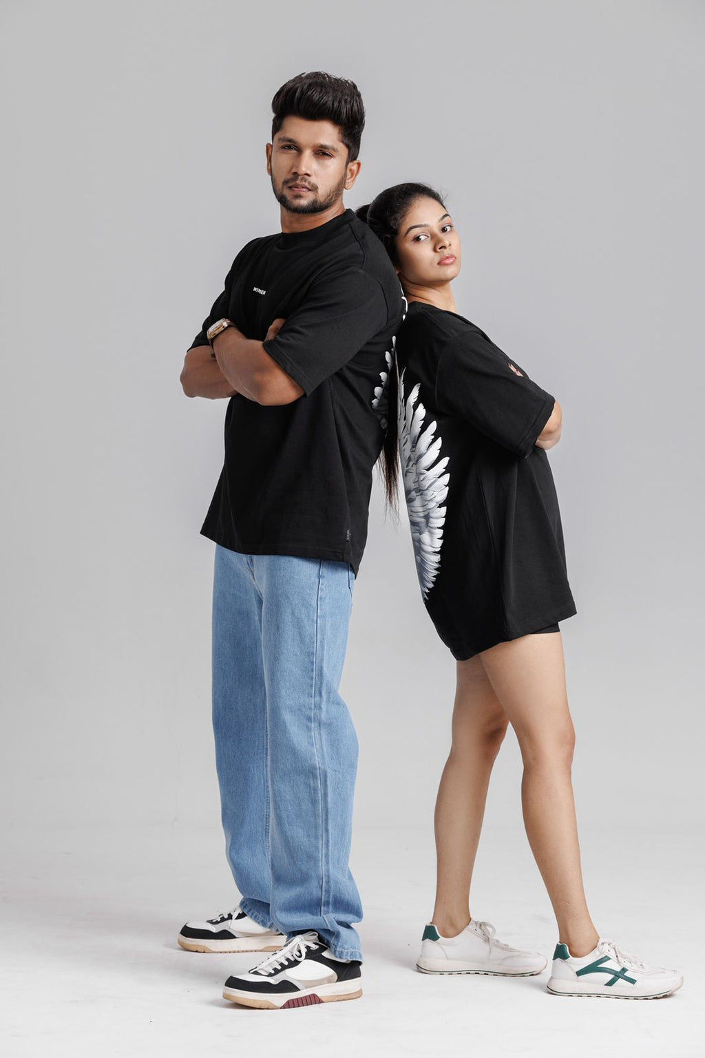 Two people wearing black t-shirts with designs, standing back-to-back against a gray background.